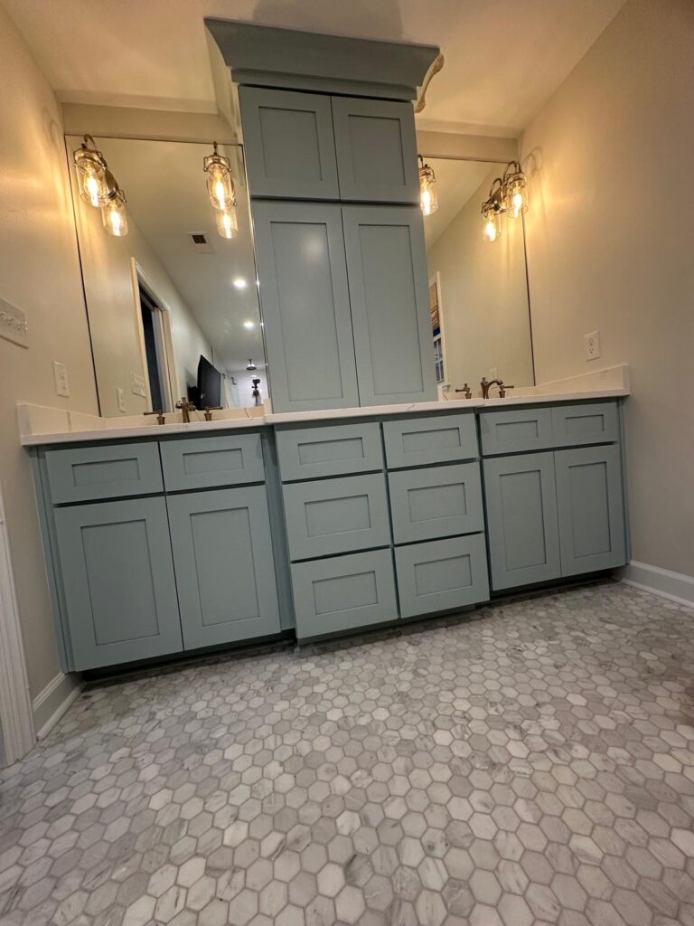 A modern bathroom with light blue double-sink cabinets, quartz countertops, hexagonal marble floor tiles, and three pendant lights above large mirrors—showcasing expert cabinet painting Charlotte homeowners love.