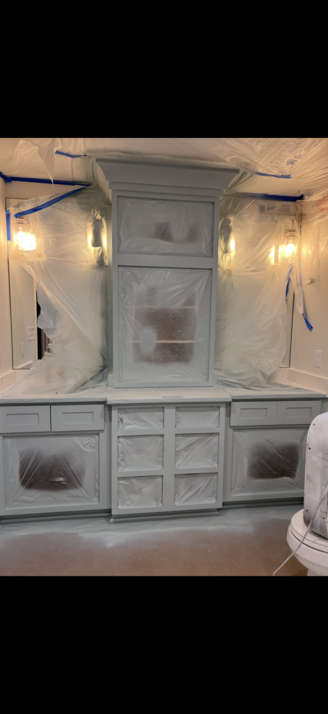 A built-in cabinet and surrounding walls are covered with plastic sheeting and painters tape for protection. The area is being prepped for cabinet painting Charlotte, and two wall sconces on either side are illuminated.