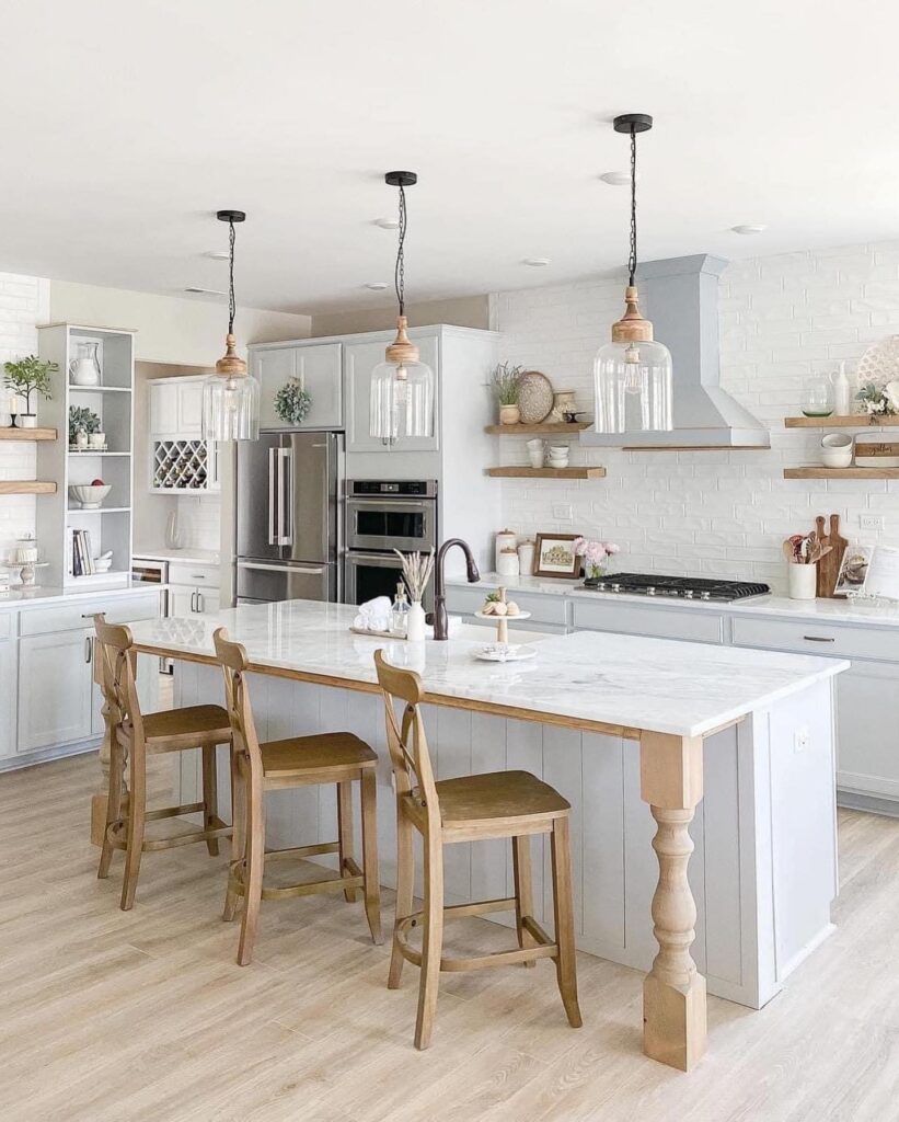Bright, modern farmhouse kitchen with white cabinets—expertly finished by cabinet painting Charlotte—a marble island with wooden stools, pendant lights, open shelves displaying decor, stainless steel appliances, and light wood flooring.
