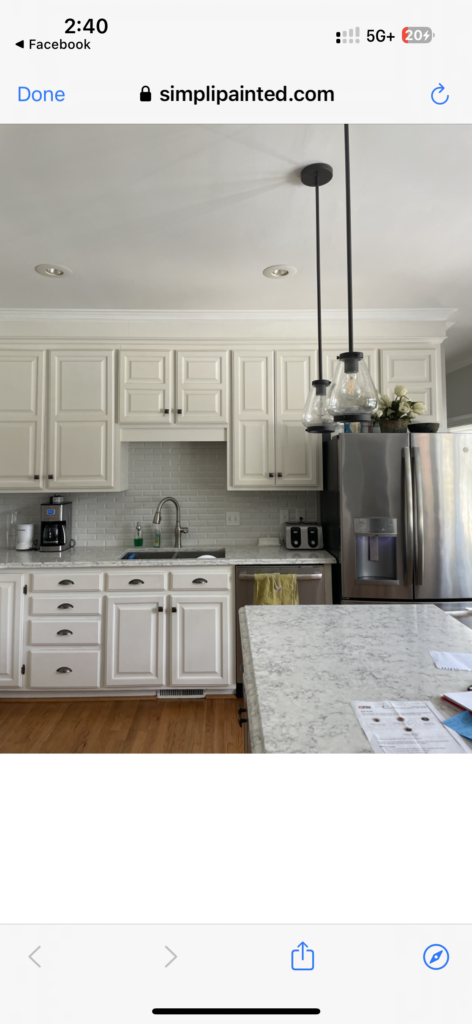 A modern kitchen with white cabinets featuring expert cabinet painting Charlotte, a subway tile backsplash, stainless steel appliances, two pendant lights, a marble island with papers and a pen, wood flooring, and under-cabinet lighting.