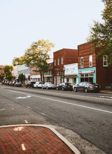 A quiet small-town street in Davidson, NC, with parked cars, brick sidewalks, and a row of storefronts and trees in the background under a clear sky.