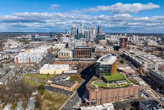 Aerial view of a cityscape with modern high-rise buildings in the background, mid-rise and low-rise structures in the foreground, and partly cloudy skies overhead—much like the vibrant transformation achieved through Cabinet Painting in Matthews NC.