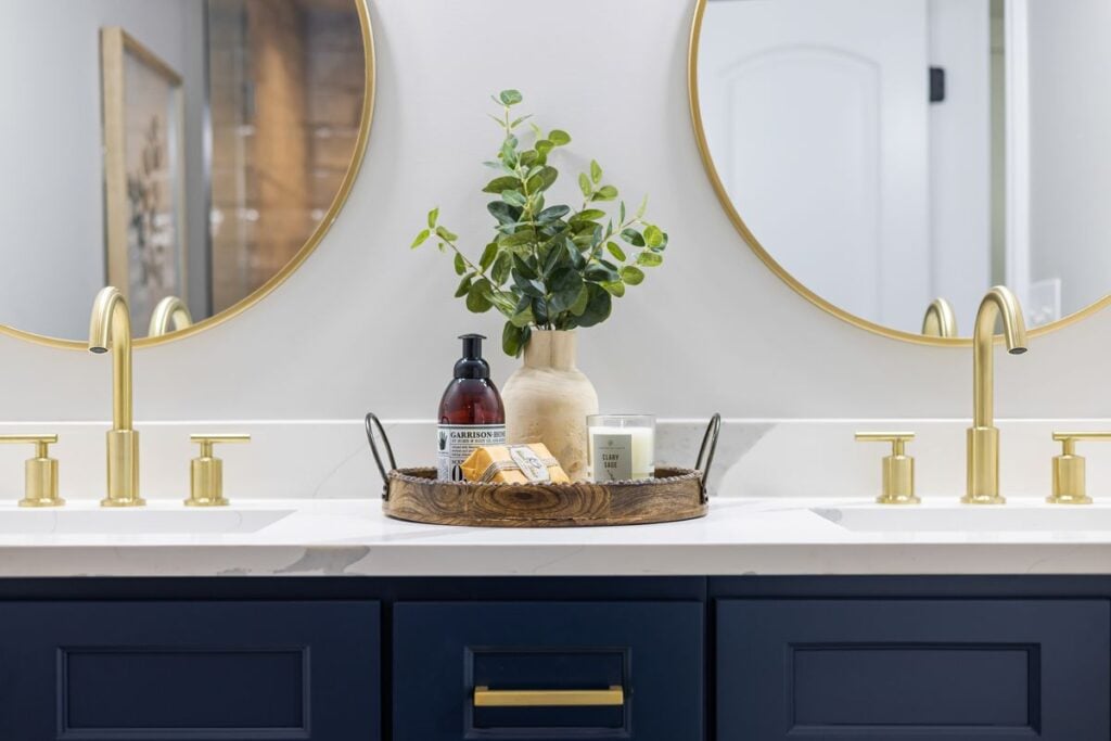 Navy double vanity with a white stone countertop, gold faucets and round mirrors