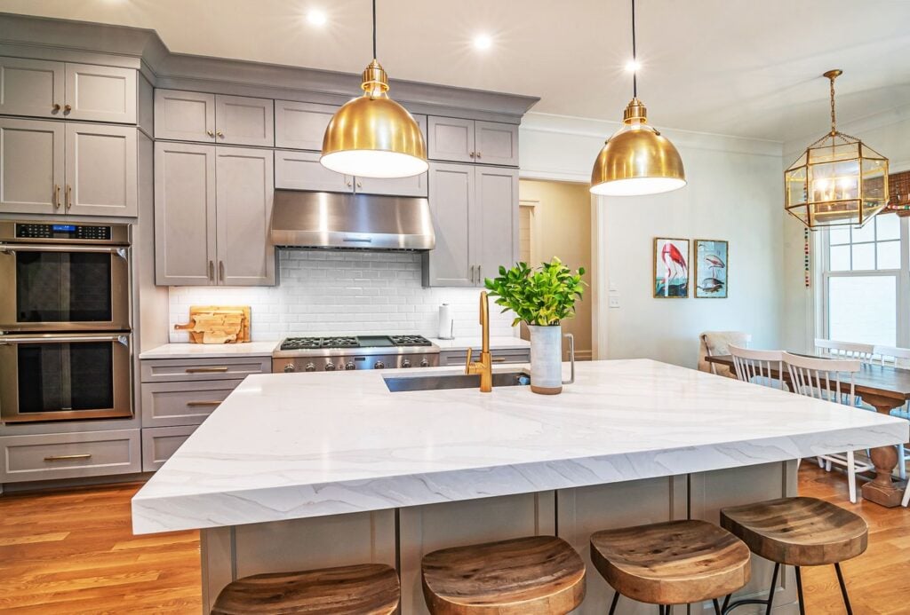 Kitchen with a large white stone island, gray cabinets and brass pendant lights