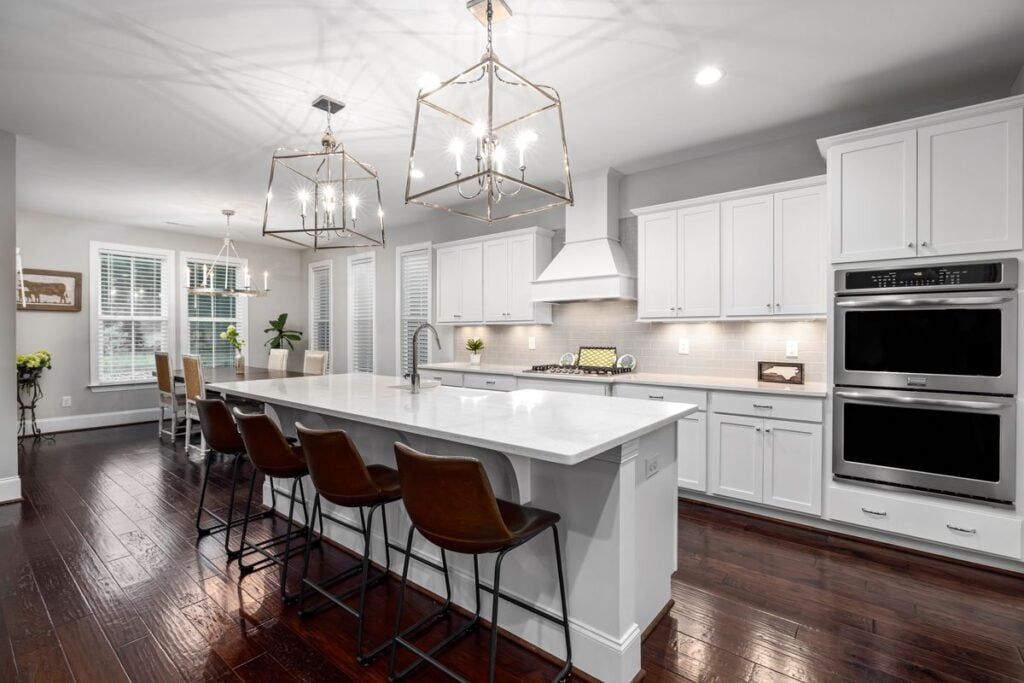 Large kitchen island with a white stone top, bar stools and lantern pendants