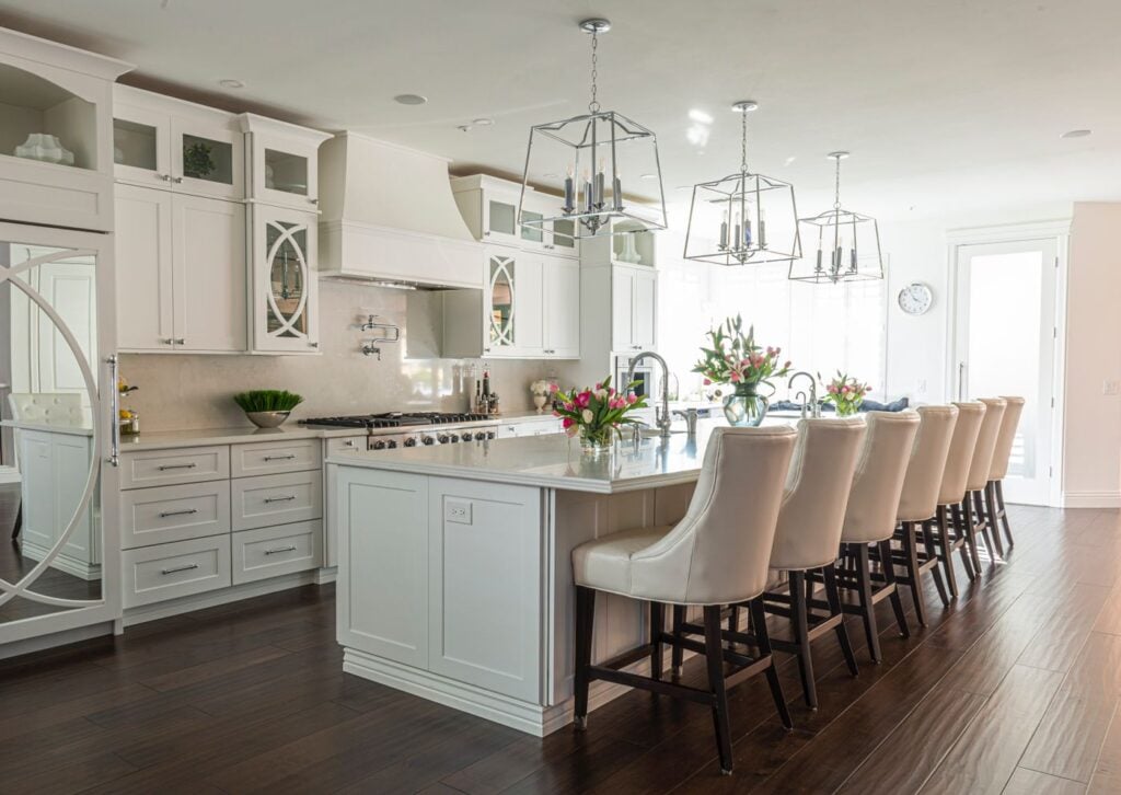 White kitchen with a long island, tufted chairs and chandeliers