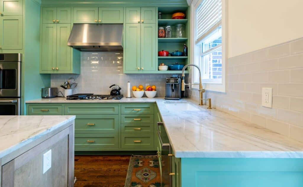 Kitchen with green painted cabinets, light stone countertops and a tile backsplash