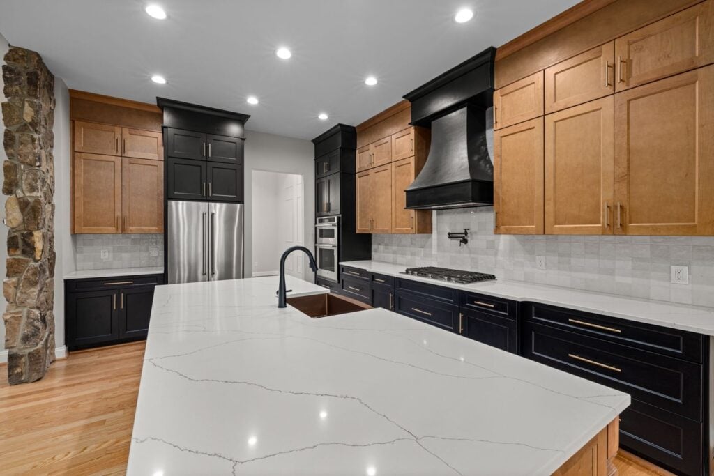 Kitchen with wood and black cabinets, a white stone island and a tile backsplash